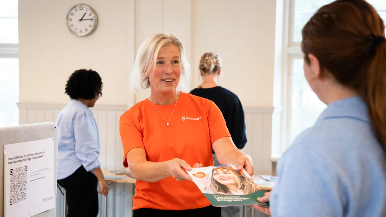 En kvinna i en orange tröja håller en bok i handen.