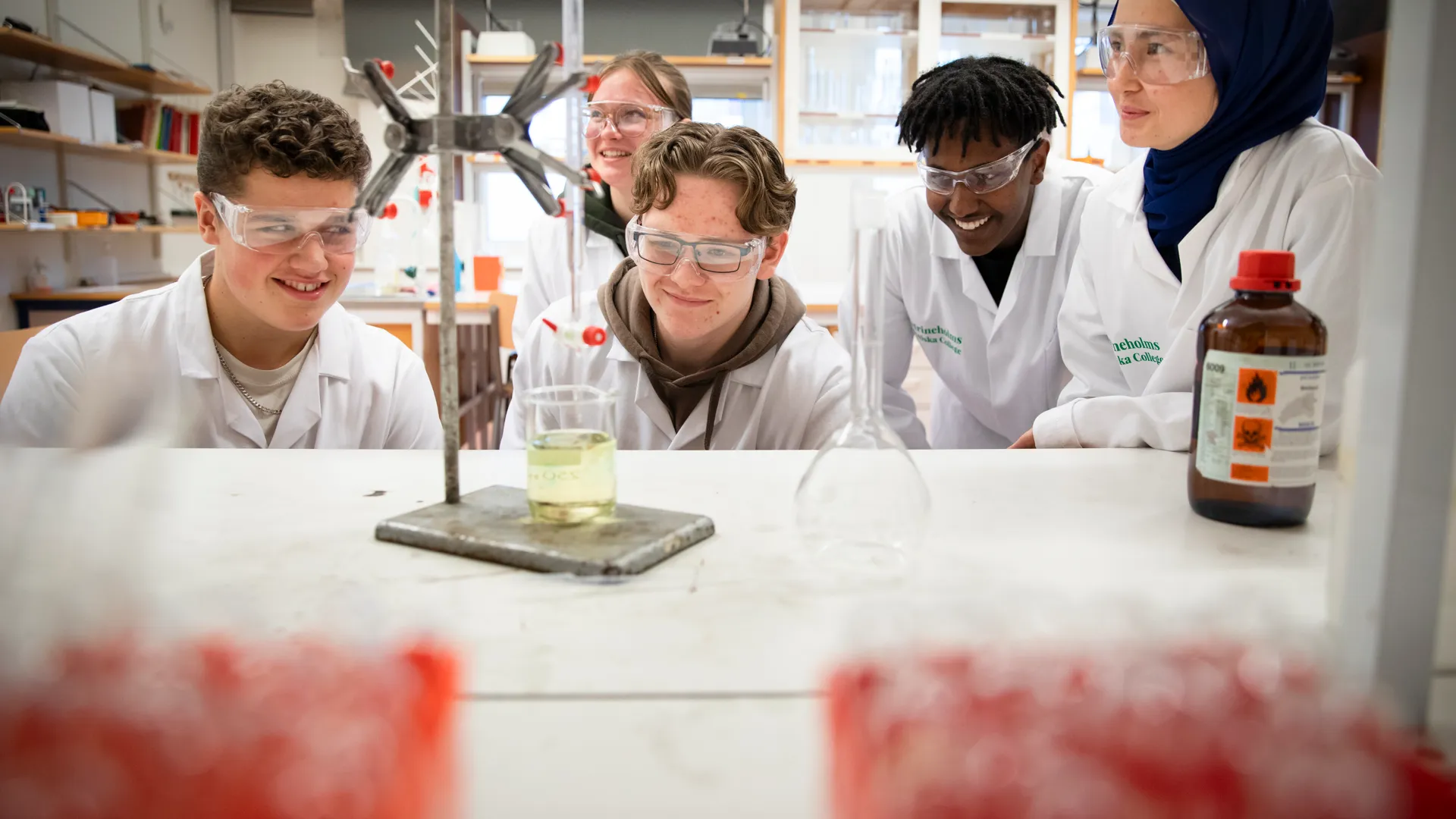 Elever i labkläder gör experiment i en kemisal.