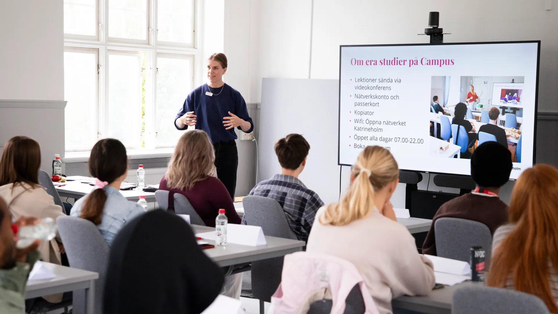 Unga vuxna studenter som sitter i ett ljust klassrum i vita och ljusgrå toner.