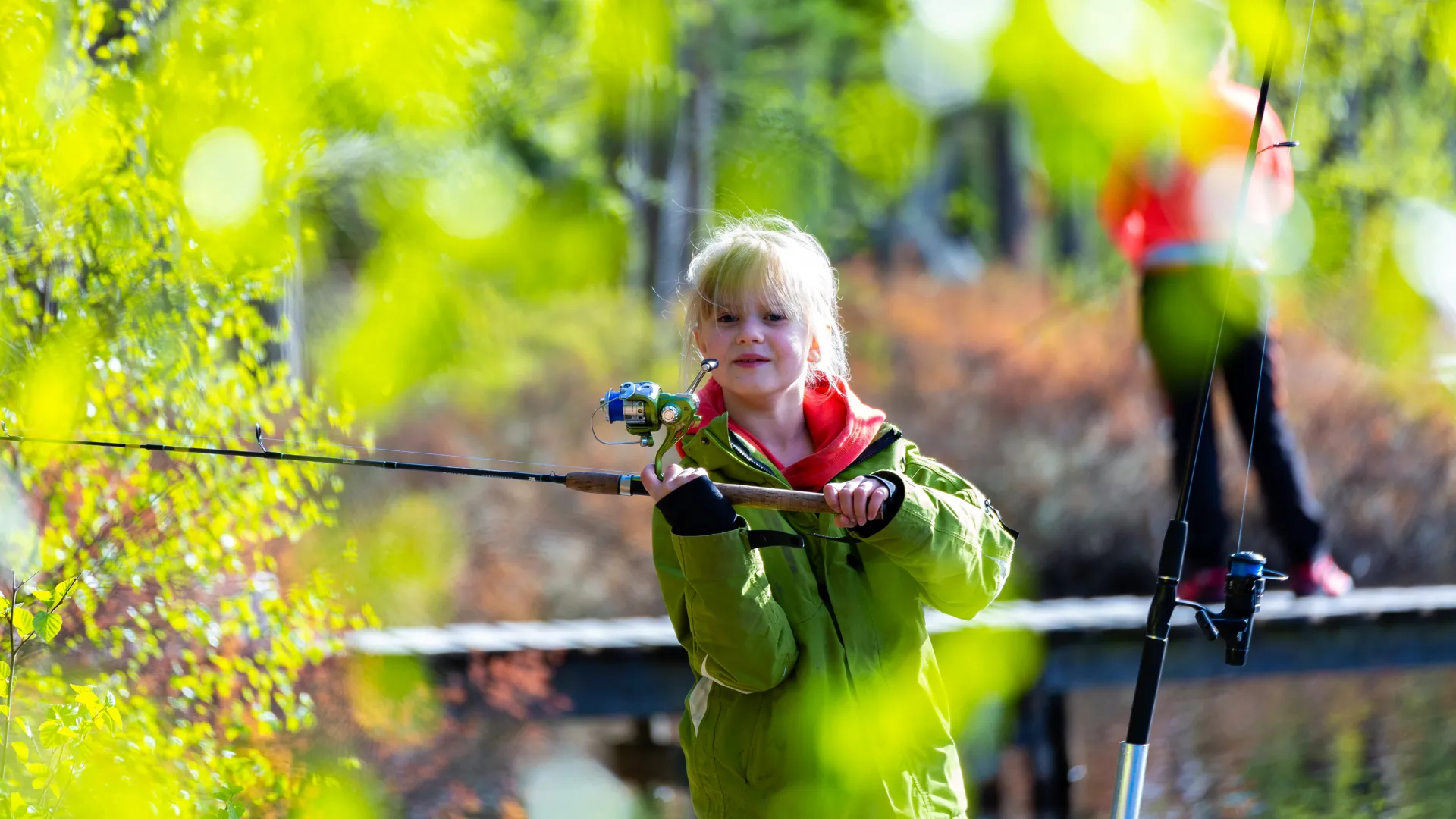 En liten flicka som står på en bro och håller i ett fiskespö.