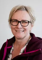En kvinna med glasögon som ler mot kameran.