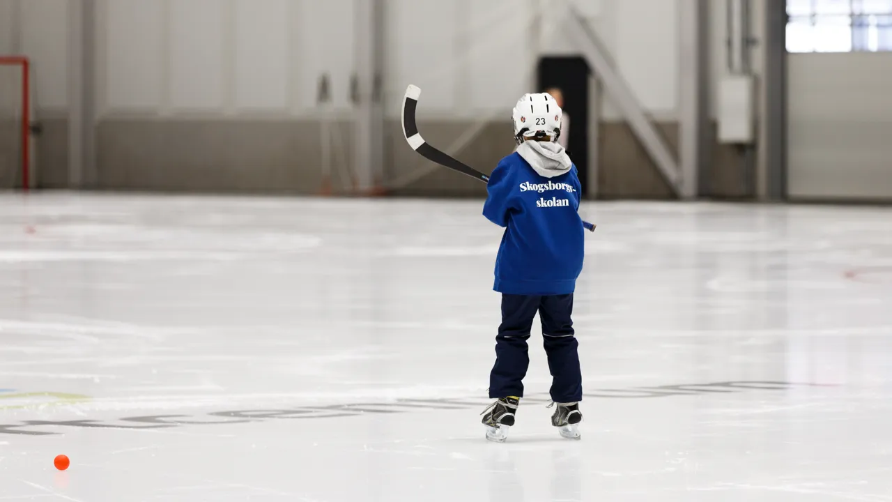 En liten pojke som spelar ishockey på en inomhusisbana.