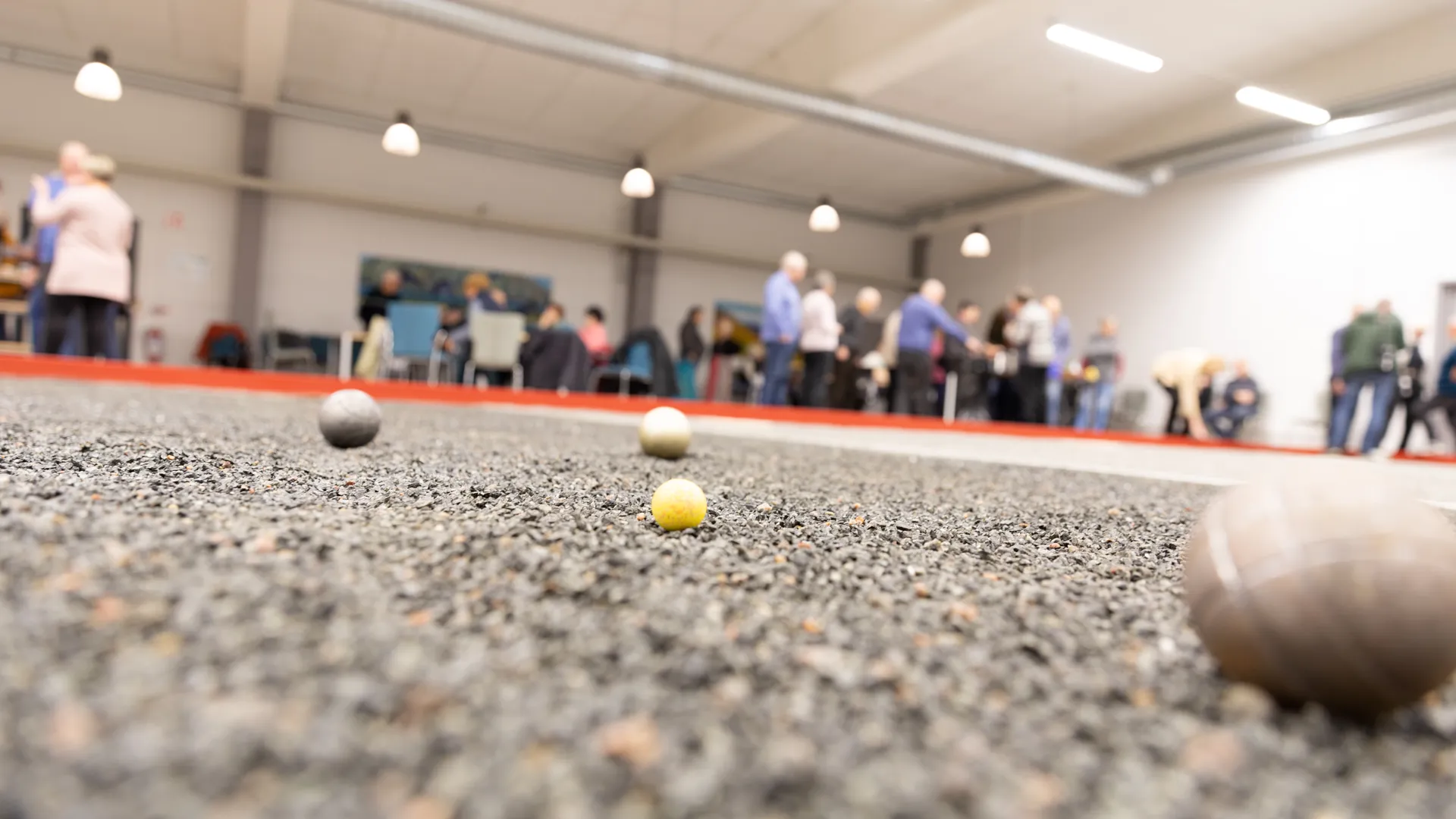 bouleklot på en boulebana i bakgrunden syns människor som spelar boule