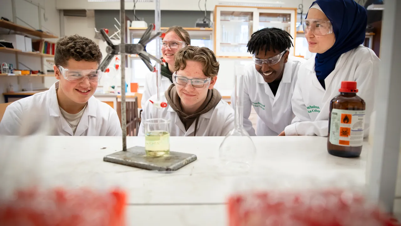 Elever i labkläder gör experiment i en kemisal.