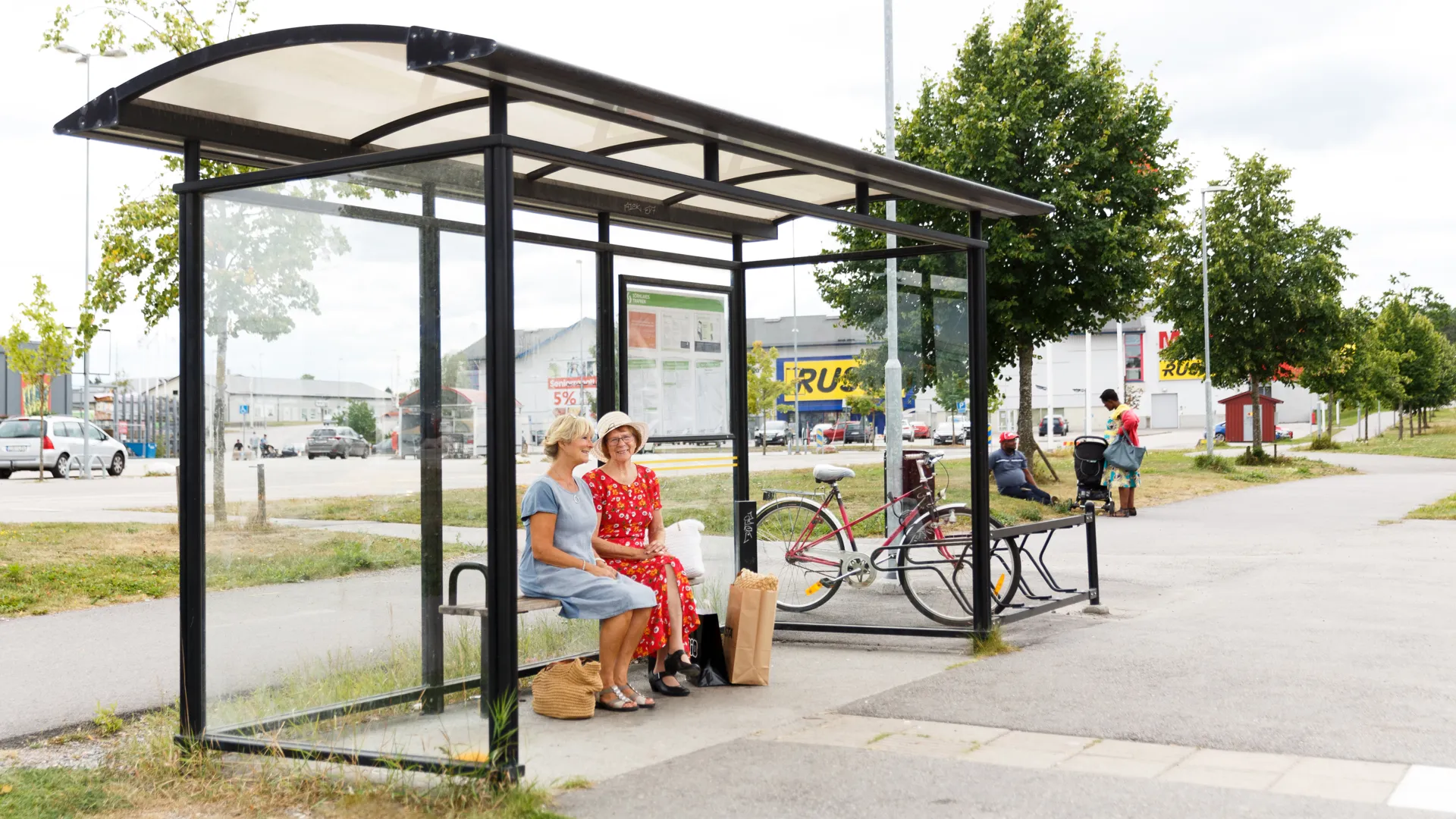 Två personer sitter och väntar på bussen på Lövåsen.