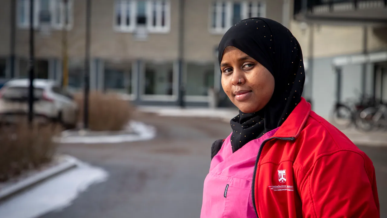 En kvinnlig undersköterska i röd jacka och rosa arbetskläder