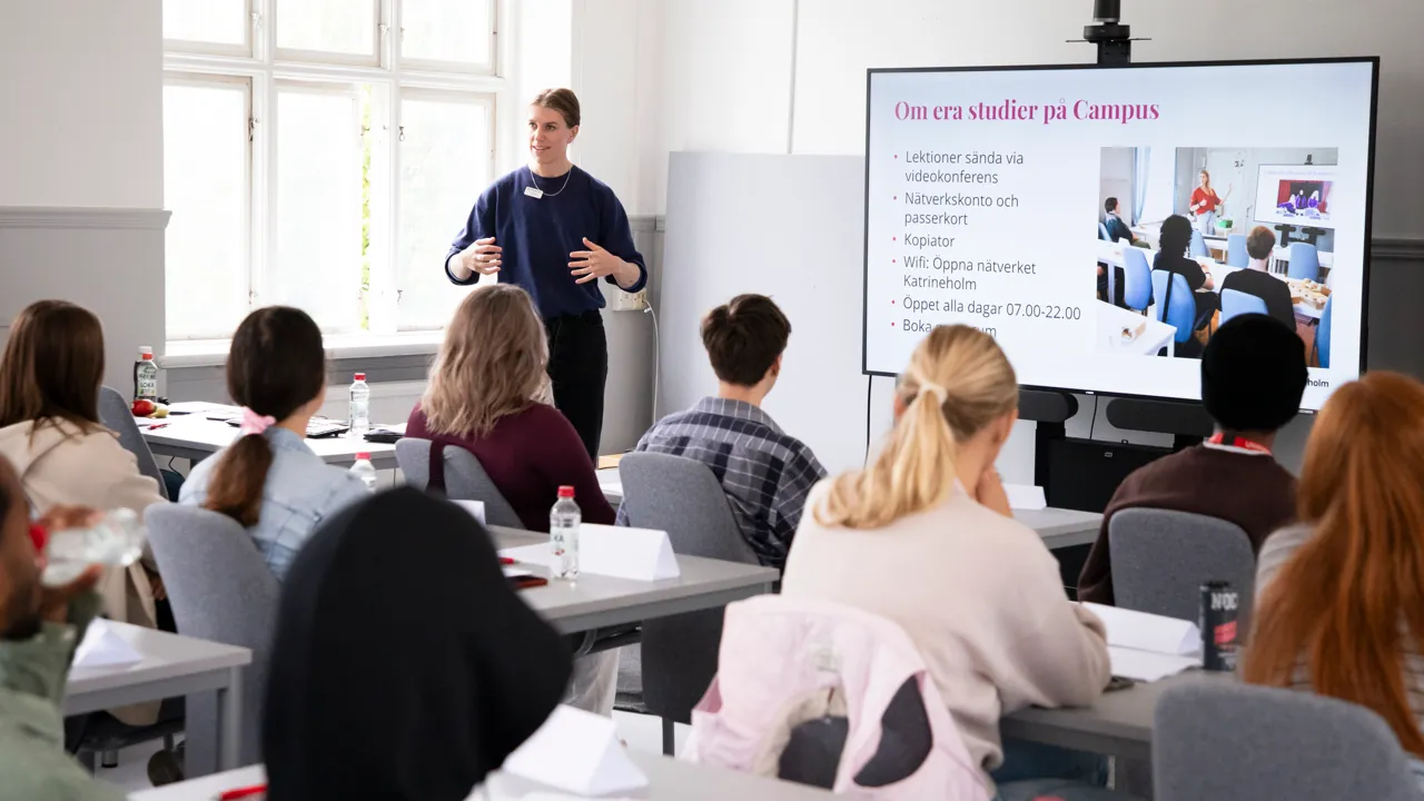 Unga vuxna studenter som sitter i ett ljust klassrum i vita och ljusgrå toner.