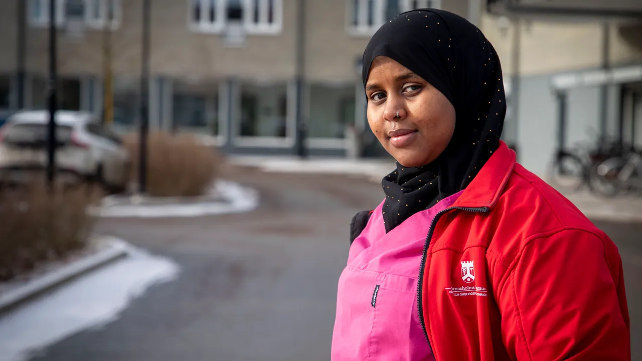 En kvinnlig undersköterska i röd jacka och rosa arbetskläder