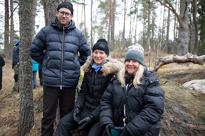 Tre av deltagarna, en lutar sig mot en trädstam och två sitter på en sten i skogen.