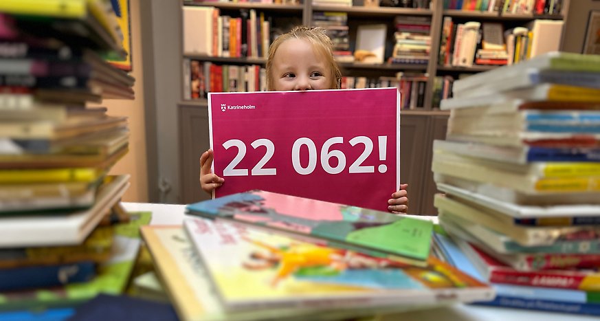 Barn som sitter bland böcker håller upp en skylt med siffran 22062 på. Det är antalet böcker som lästs under projektet Hela förskolan läser.