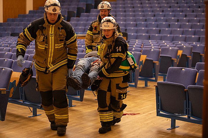 Bilden visar en övningssituation där räddningstjänst och sjukvård, efter att polisen säkrat lokalerna, ger vård och evakuerar skadade från aulan.