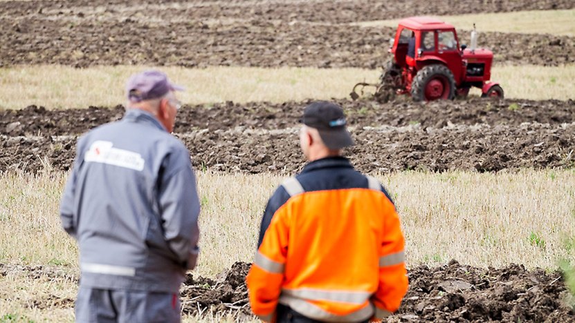 Två lantbrukare med en traktor på ett fält i bakgrunden.