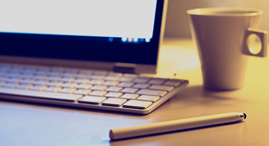 En bild på en dataskärm, ett tangentbord, en penna och en vit kopp.