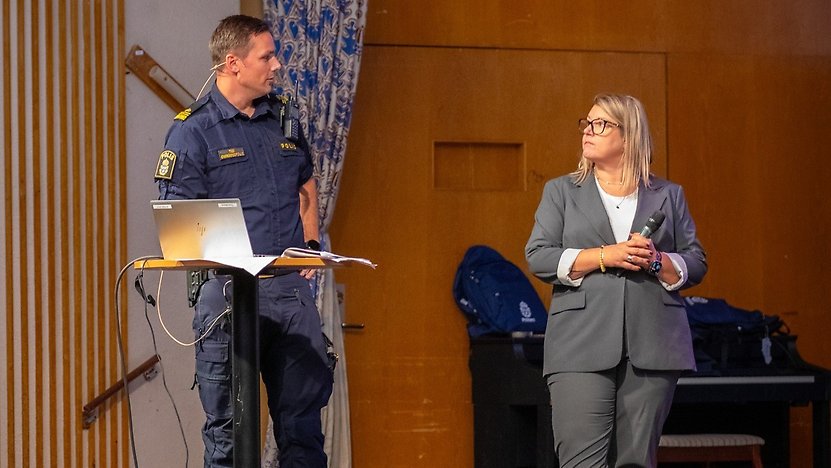 En manlig polis och en kvinna står på en scen.